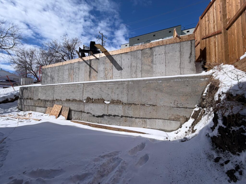 Tiered cast-in-place concrete retaining wall engineered for residential slope stabilization in Calgary, Alberta, during winter construction.