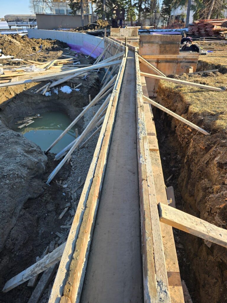 Precision concrete formwork and site preparation for a structural retaining wall footing in Calgary, showing professional engineering reinforcement.